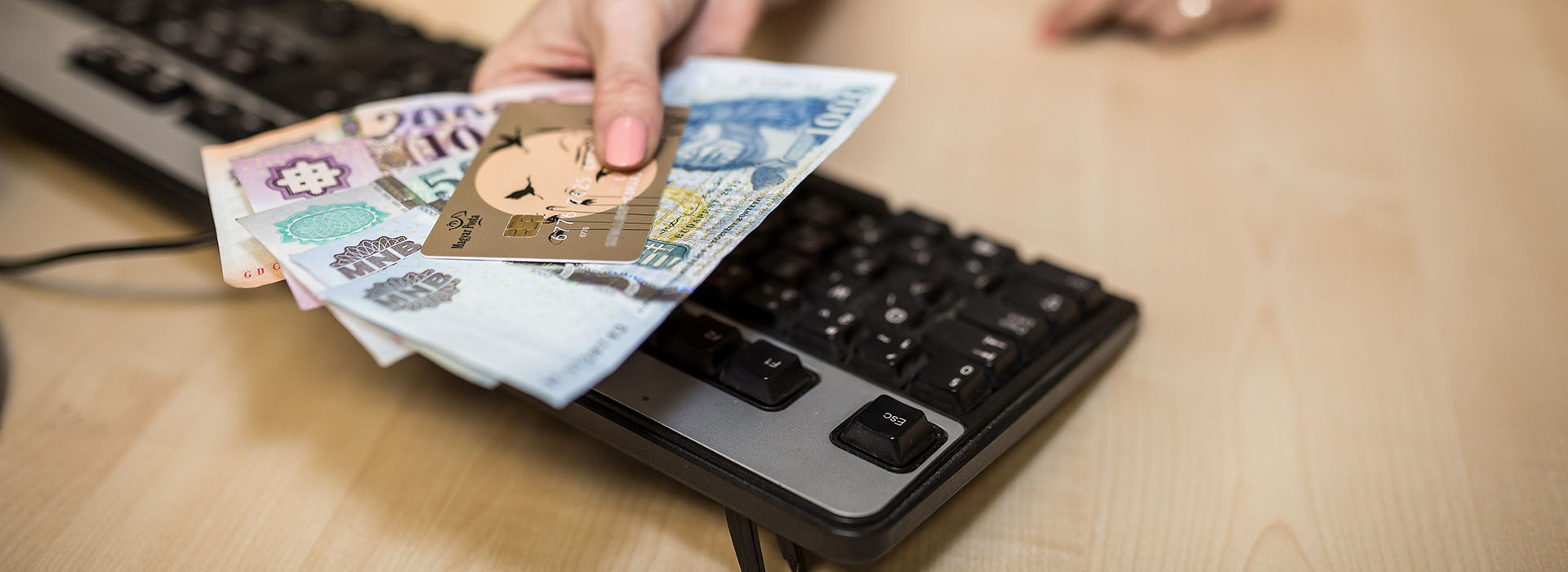 a képen egy billentyűzet látható, felette egy kéz tart egy hitelkártyát és kézpénzt
